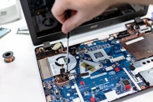 Home Hand repairing a laptop motherboard with a screwdriver, highlighting tech maintenance.